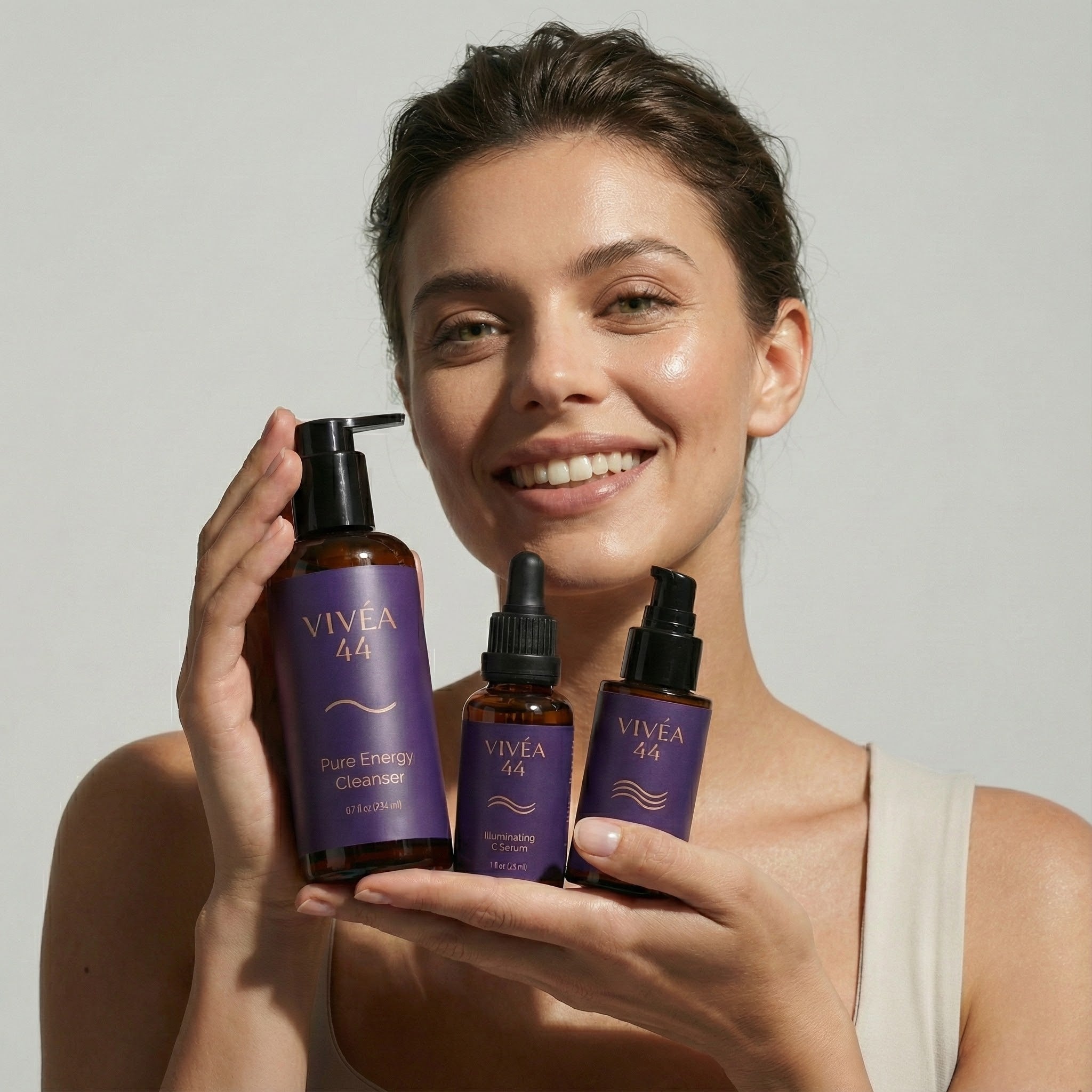 Woman holding three bottles of VIVE 44 skincare products against a plain background
