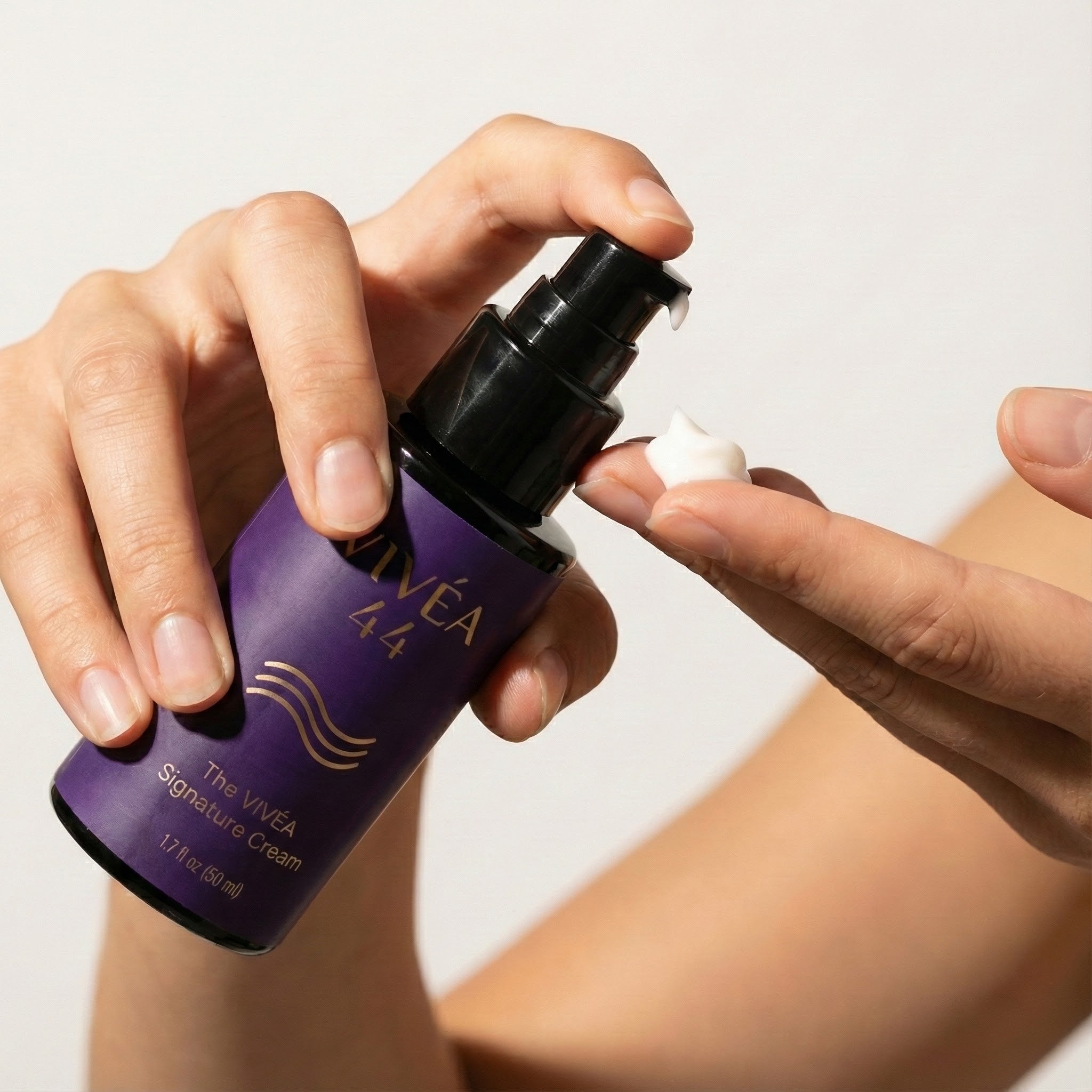 Hand holding a Vivea 44 signature cream bottle on a neutral background