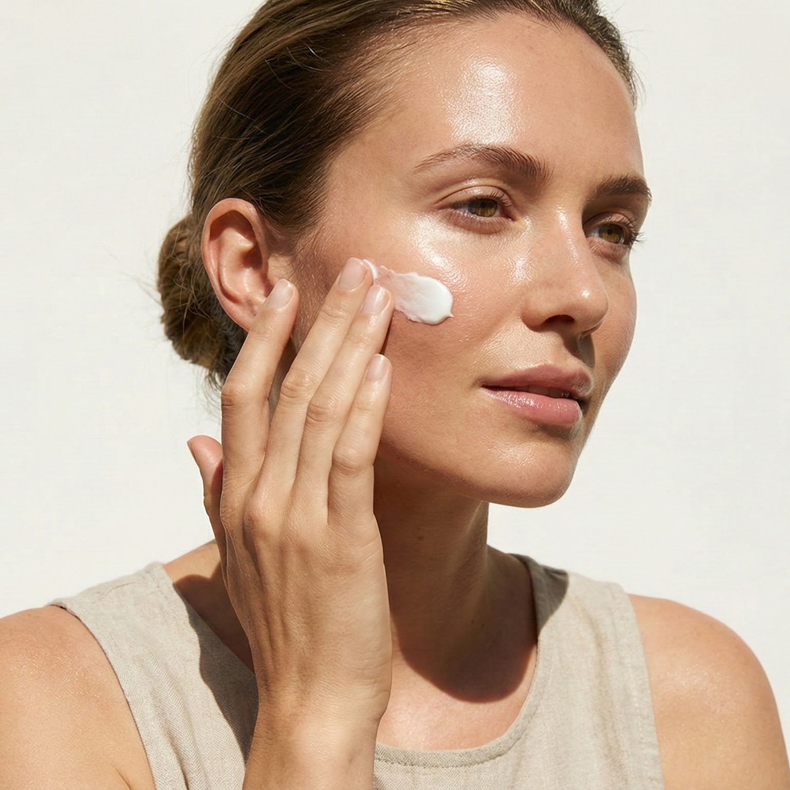 Woman applying Vivea 44 signature cream to her face against a plain background