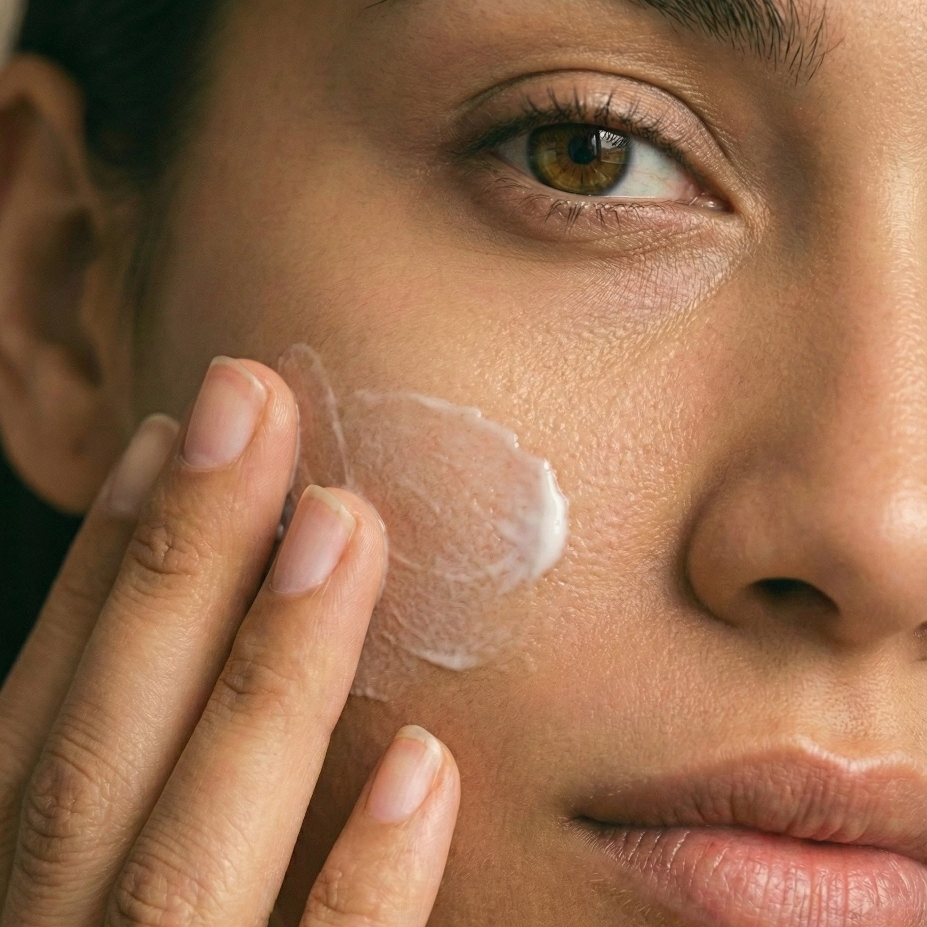 Close-up of a person applying a skincare product to their face.
